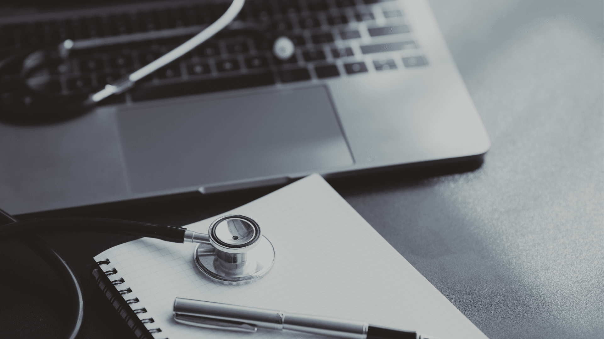 Stethoscoop en pen op een notitieblok naast een open laptop